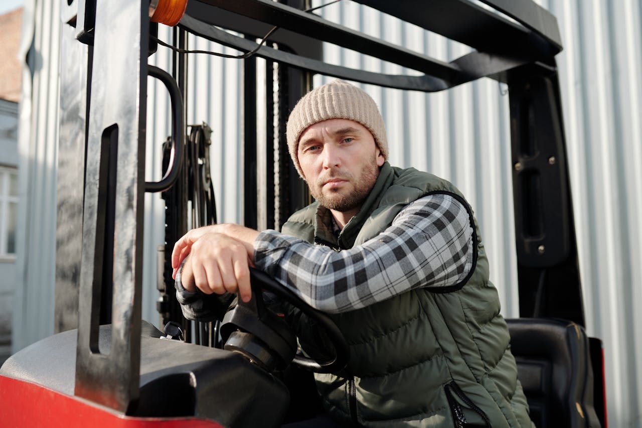 Adult male forklift operator in casual wear working outdoors. Sunlit environment.